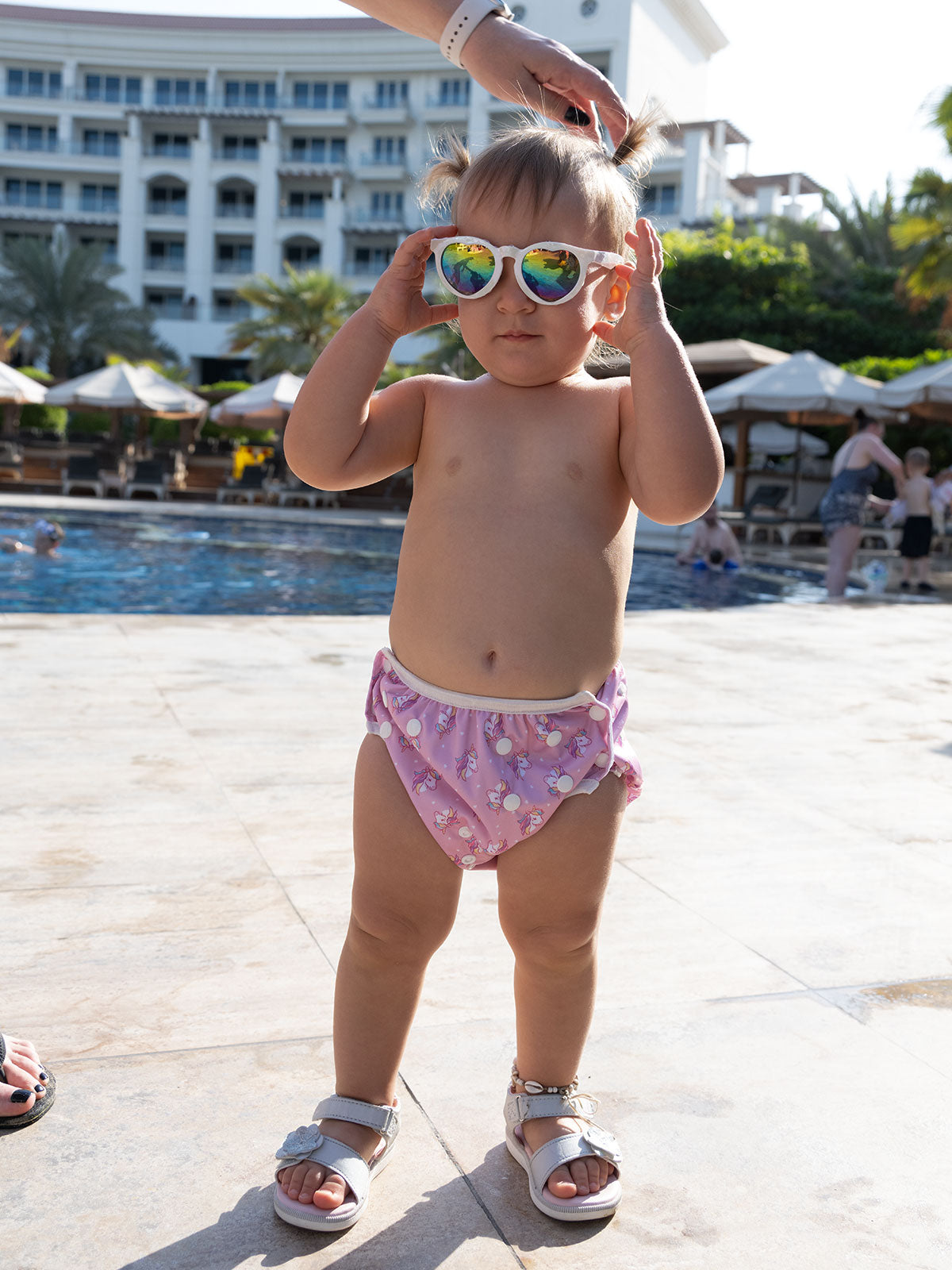 Baby steht am Poolrand und trägt eine Sonnenbrille sowie eine Baby
Schwimmwindel