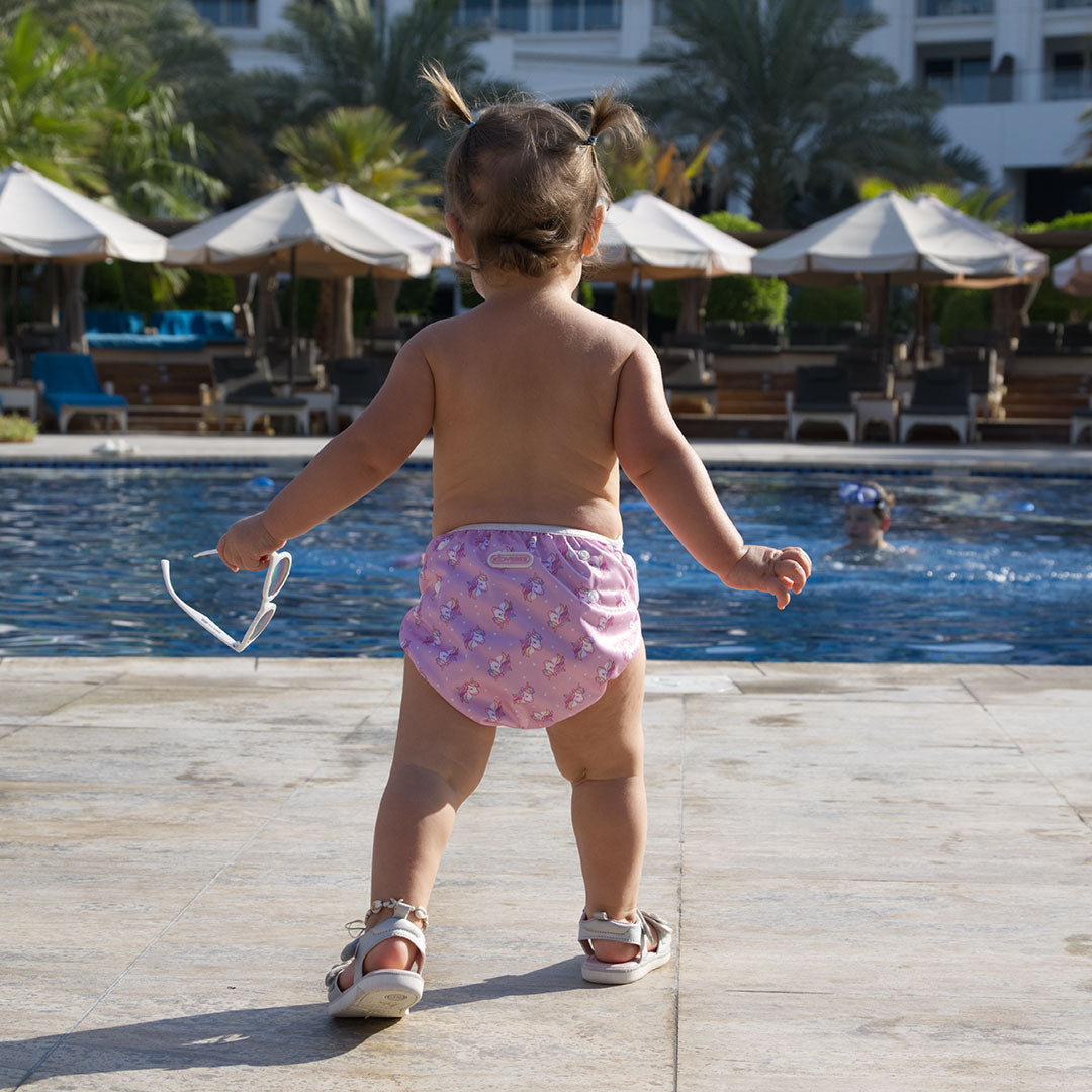 Baby steht am Poolrand und trägt eine rosafarbene Schwimmwindel mit Einhorn-Motiven
