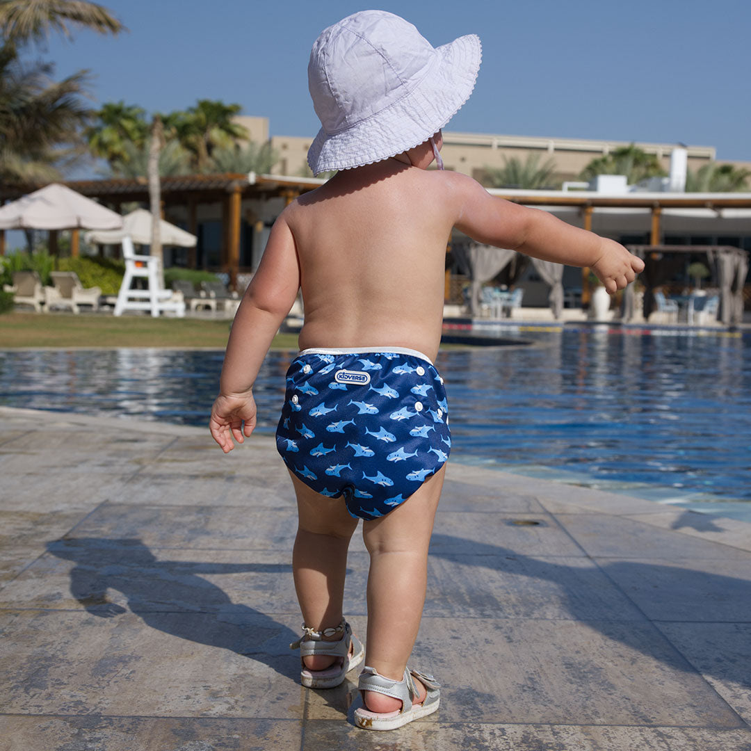 Baby steht am Poolrand und trägt eine blaue Schwimmwindel mit Hai-Motiven