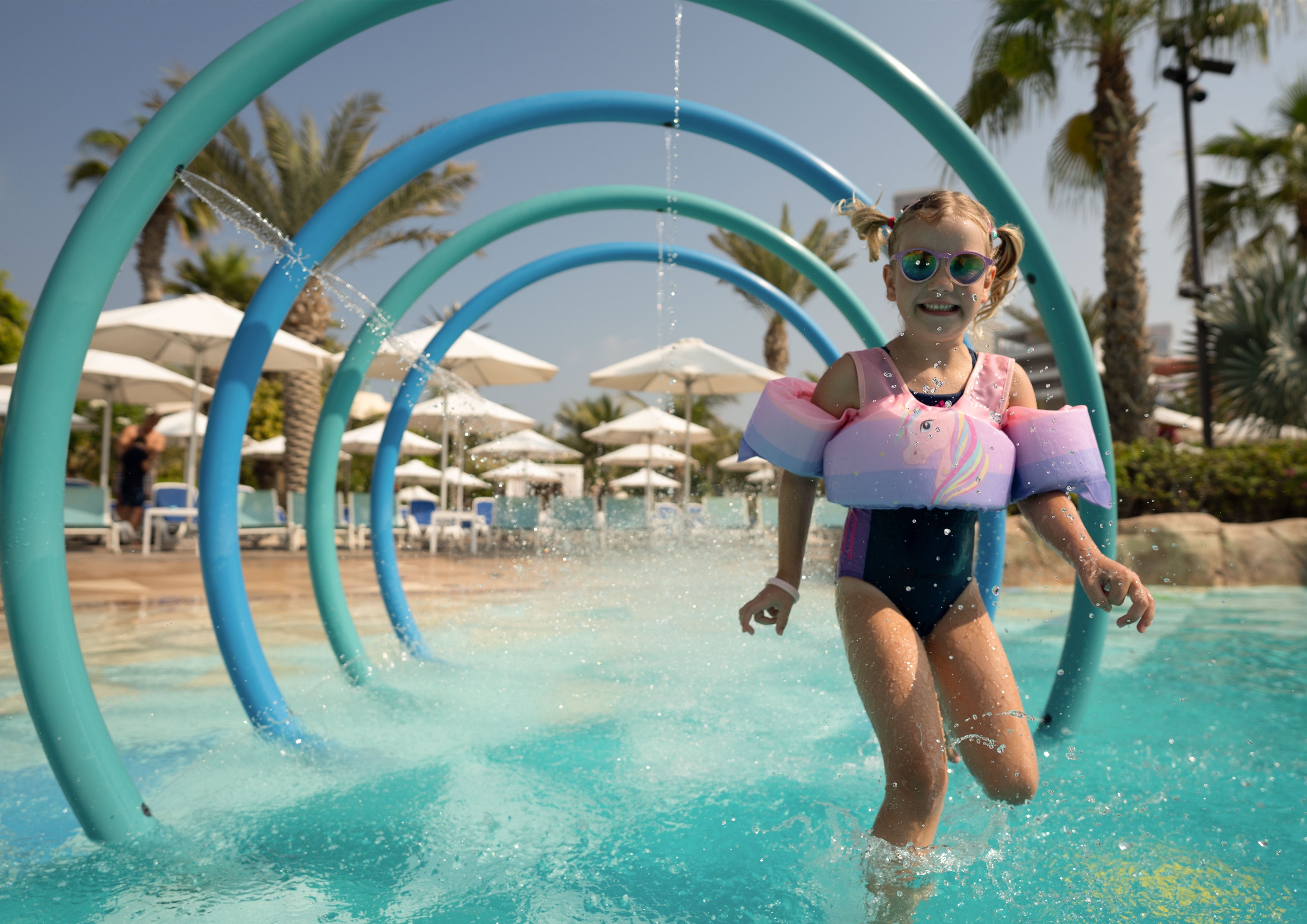Kind trägt eine Schwimmweste mit Schwimmflügeln, im Hintergrund ist ein Wasserpark zu sehen